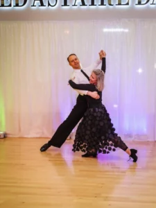 Best Time to Start Dance Lessons: A couple practices ballroom dancing together on a wooden dance floor in elegant black-and-white outfits.