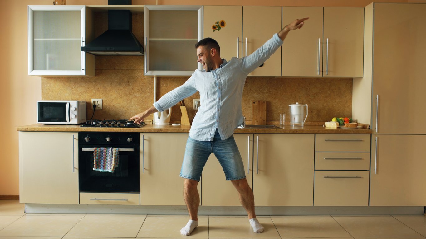 A young man dancing in his kitchen to destress.