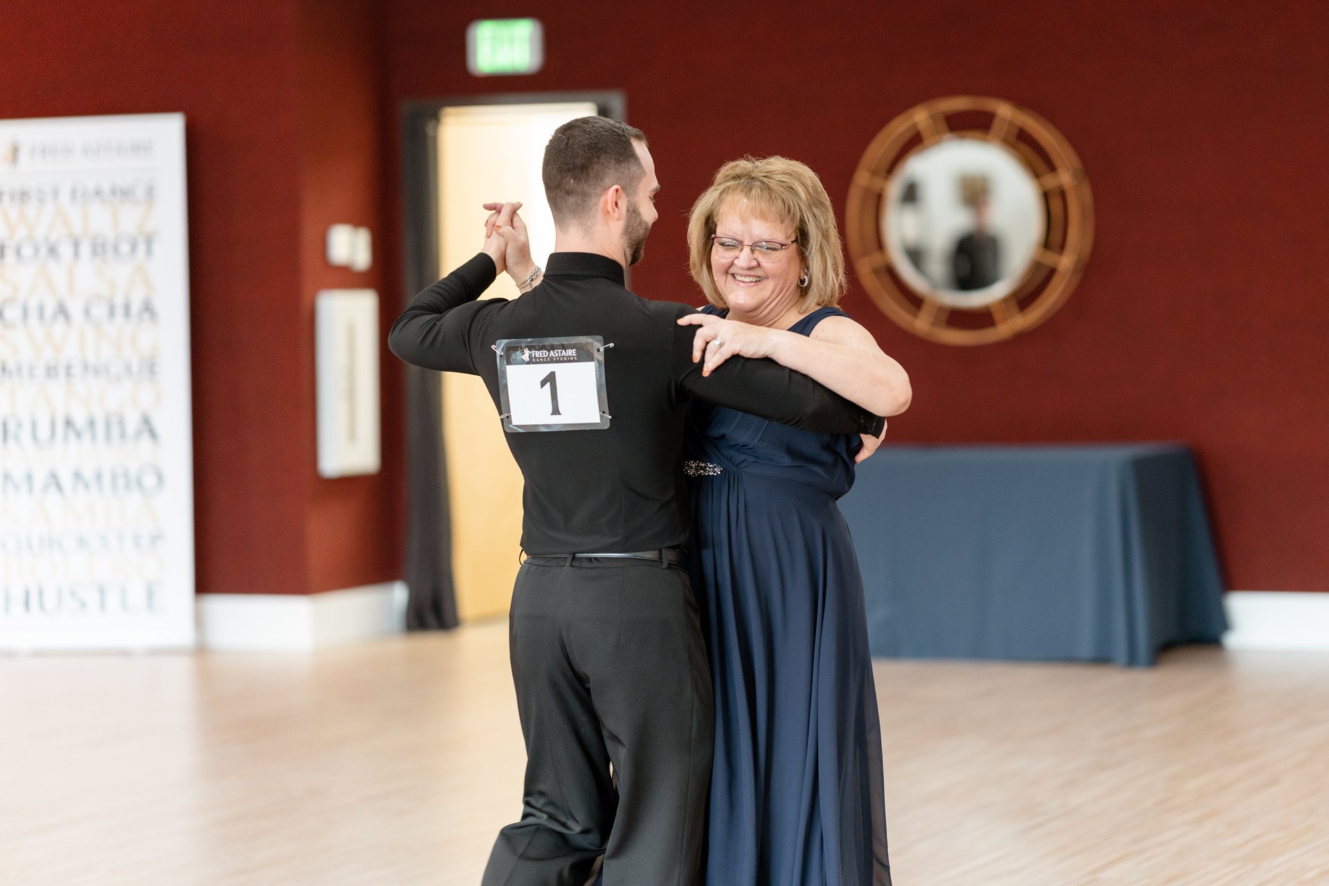 A woman in a floor length blue dress dances and laughs with her instructor at the Fred Astaire Boise dance studio.