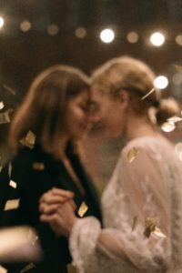 Two young women, newlywed, dancing with confetti floating around them.