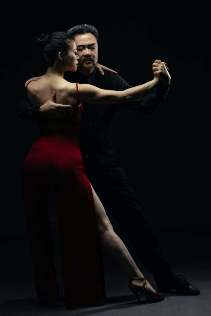 Man and woman performing the tango. Black background.