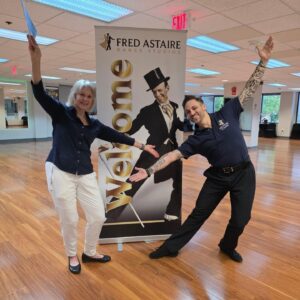 Adult student and instructor posing in a dance studio beside a welcome banner for ballroom dance lessons in Washington.
