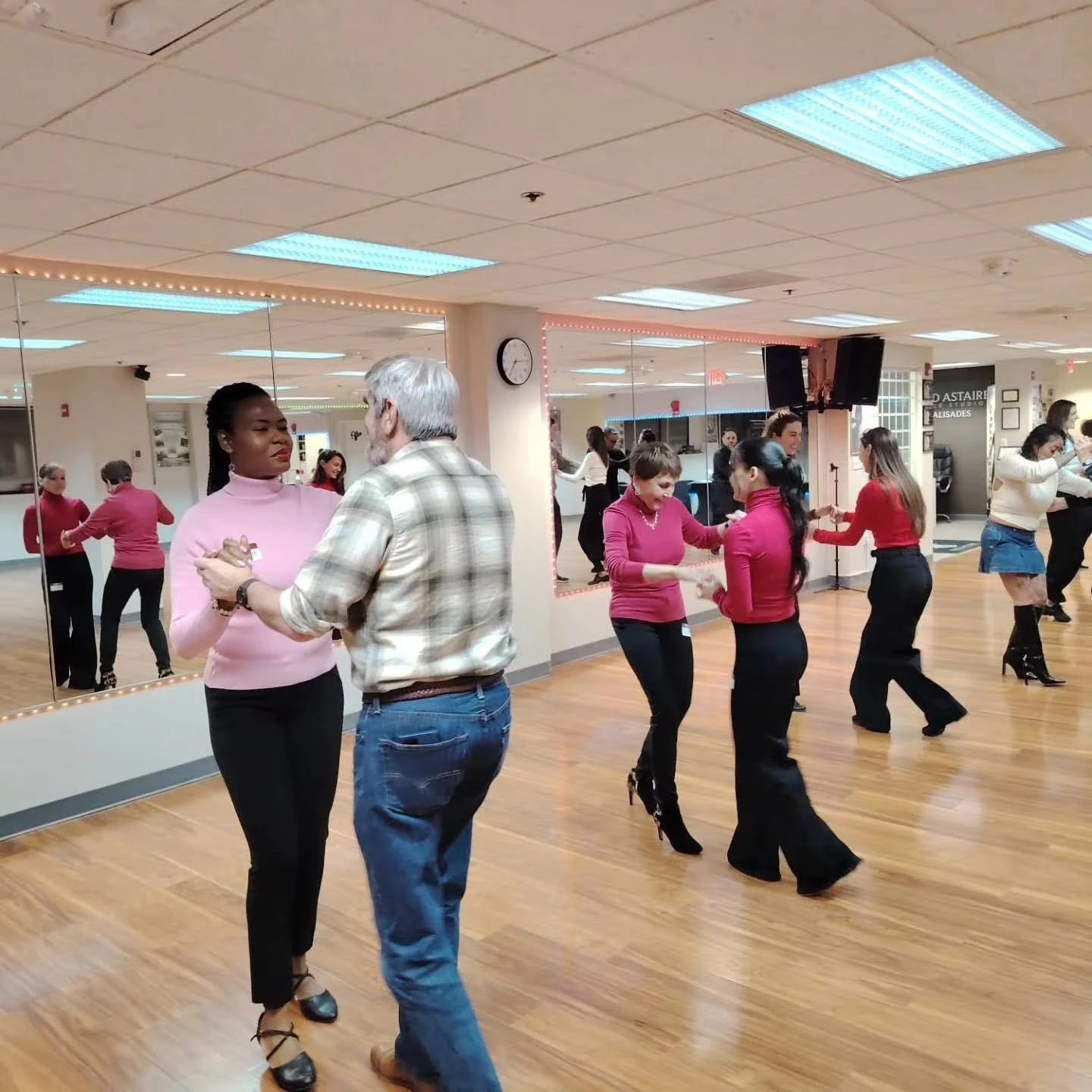 Students participate in Private Dance Lessons in Washington at a professional dance studio, practicing partner dance techniques with instructors on a spacious hardwood floor surrounded by mirrors.