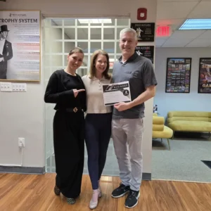 Three adults pose at a dance studio with a beginner achievement certificate, illustrating How Much Adult Dance Lessons Cost and the value of starting dance lessons.