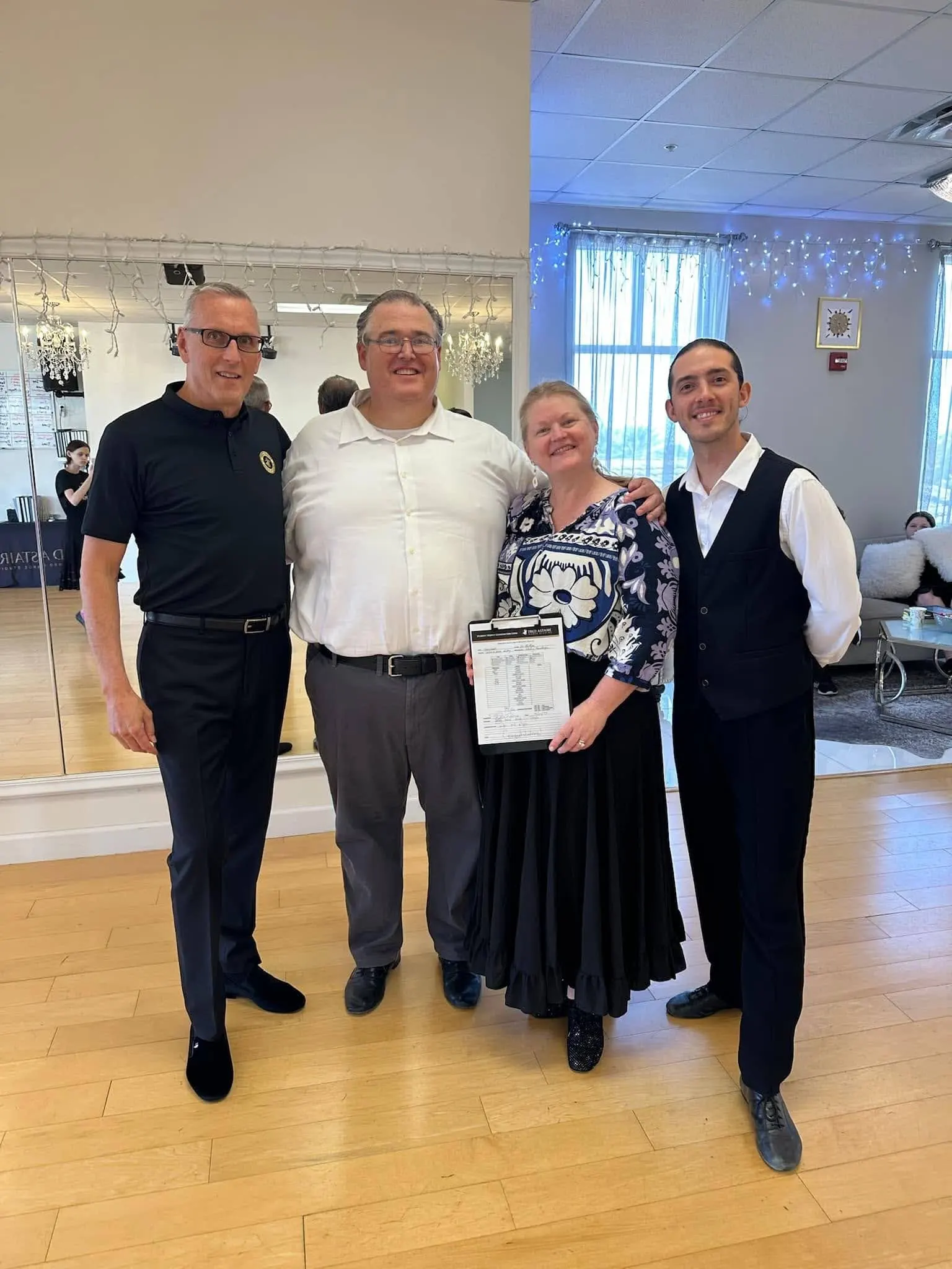 Four adults smiling together in a dance studio after completing couples dance lessons in Orlando, with one participant holding a dance score sheet.