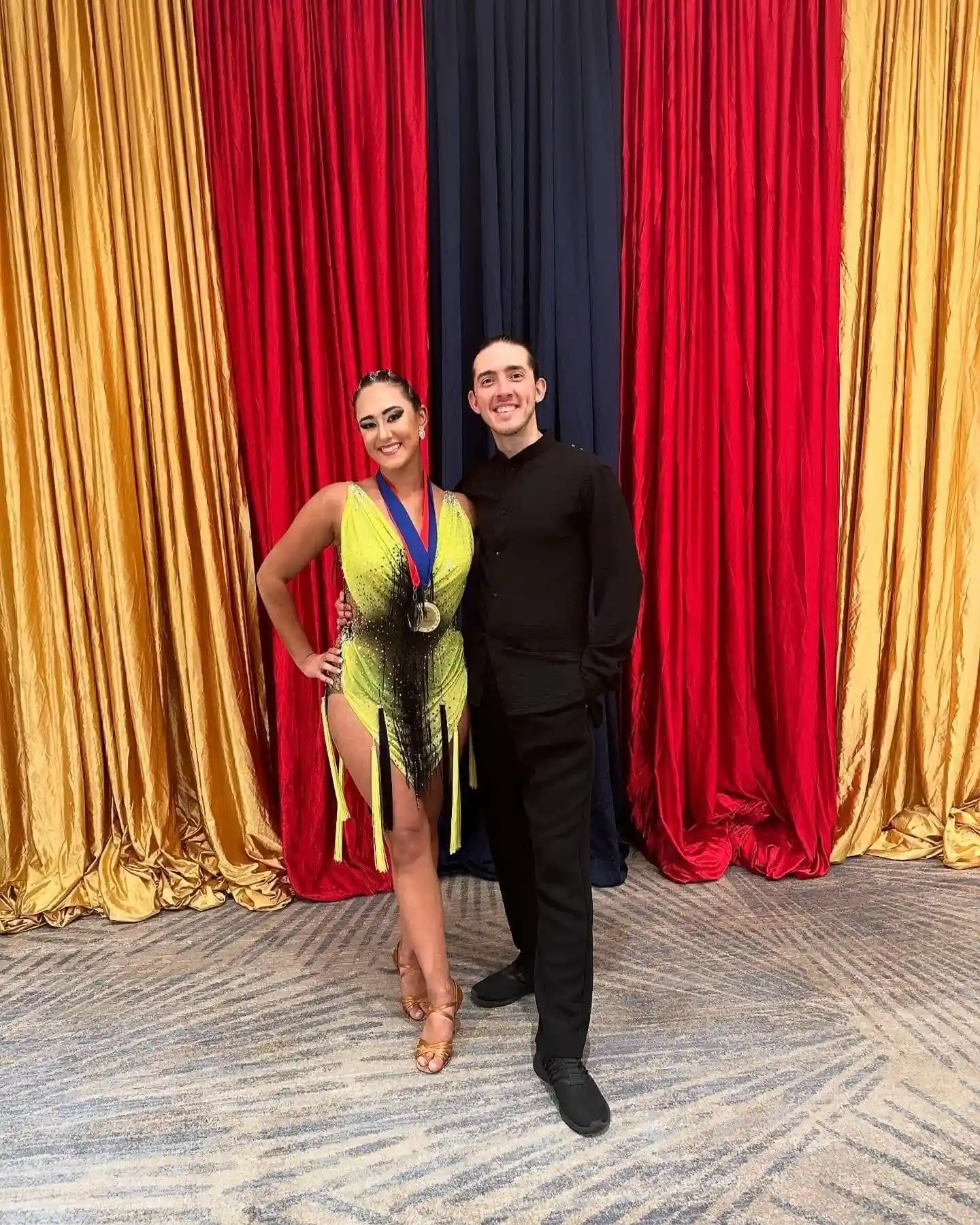A ballroom dance pair posing in front of colorful red, gold, and black curtains, highlighting a private dance lesson in Orlando.