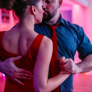 woman in red dress and man in blue shirt and red tie take mambo dance lessons.