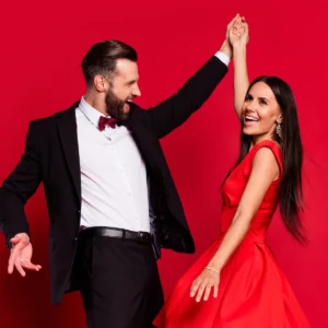 Young couple in red dress and tuxedo taking Rumba dance lessons in Durham.