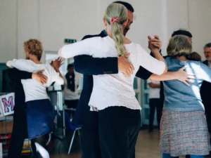 A group of adults practicing ballroom dancing in a sunlit indoor studio, capturing lindy hop vs east coast swing dance differences.