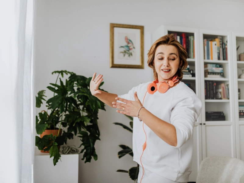 A woman learns how to practice dancing at home in her living room while listening to music on her headphones.