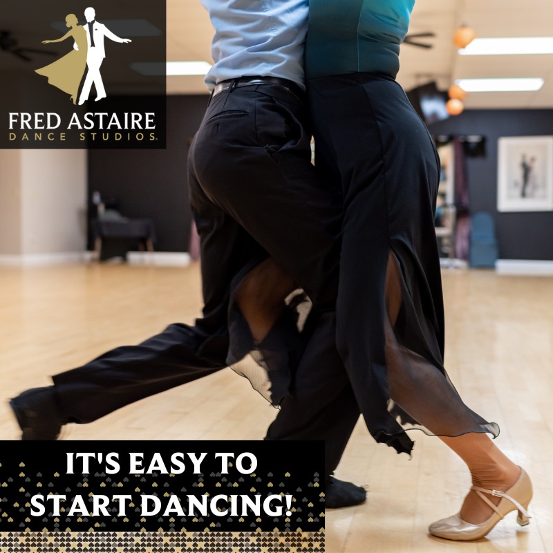 Close-up of two dancers performing ballroom dancing at Fred Astaire Dance Studios, showcasing synchronized footwork on a polished wooden floor with studio decor and a visible logo in the background.