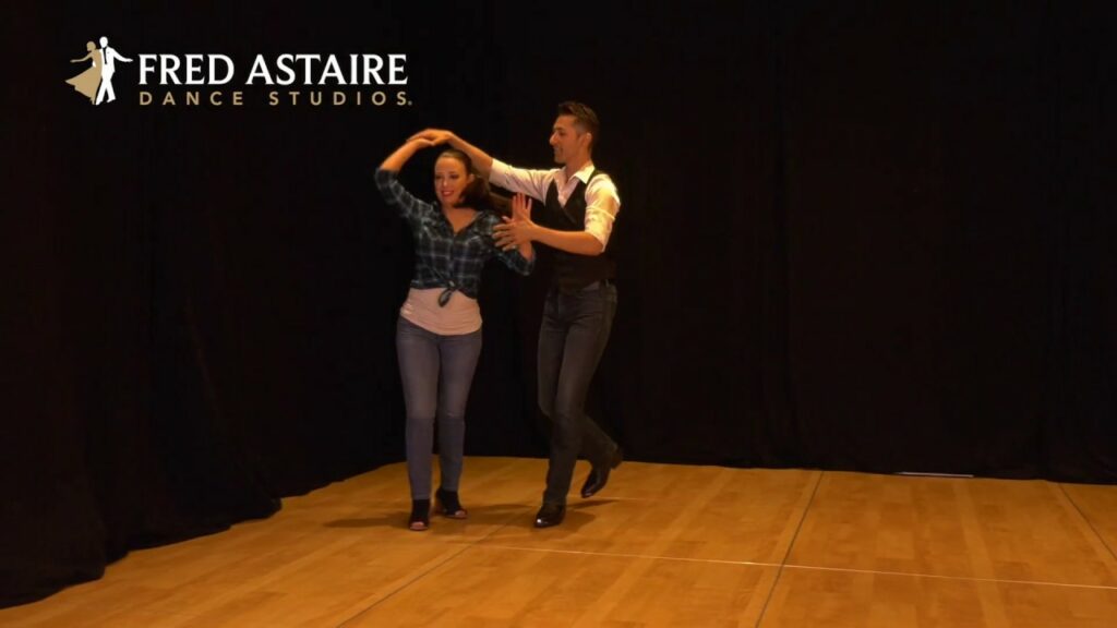 A couple country dancing on a stage with black curtains behind them. Fred Astaire Dance Studio logo in top left corner.