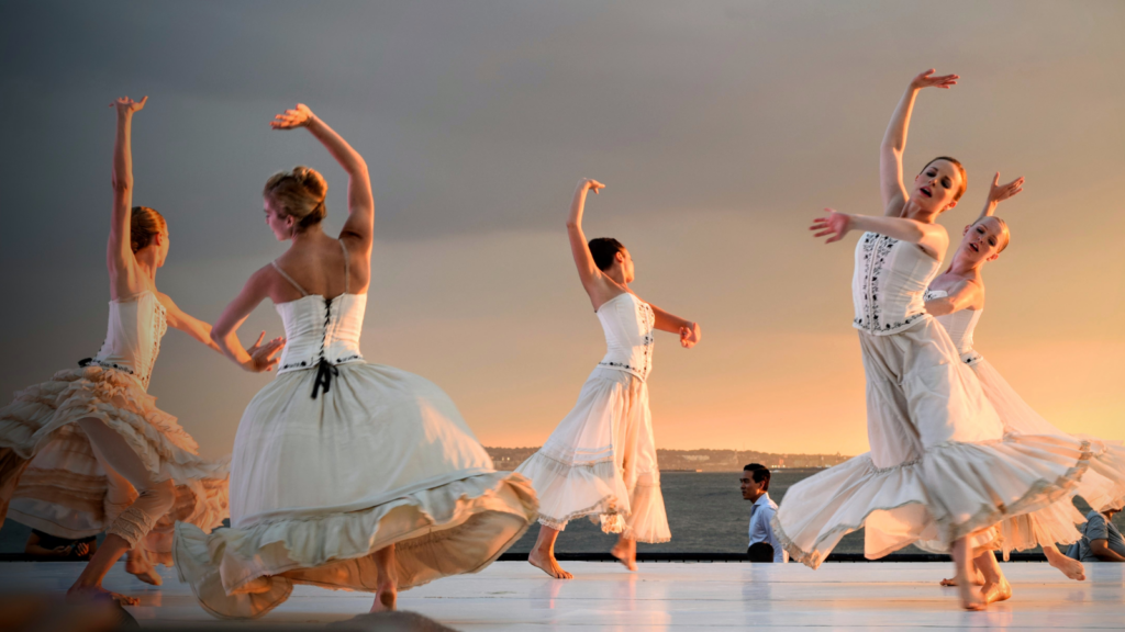 A Polka performance by five dancing women in white dresses on a stage.