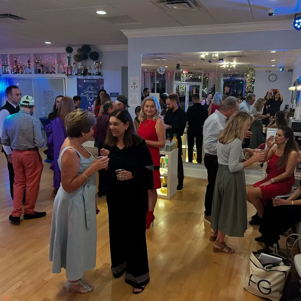 Adults socializing and enjoying an event at a dance studio, with people mingling, chatting, and celebrating after taking dance lessons for adults.