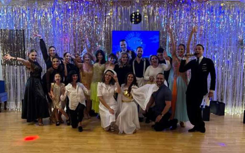 Group of dancers in ballroom attire posing together on a decorated dance floor