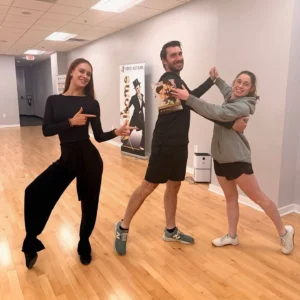 Three adults smiling and practicing dance poses in a ballroom studio, demonstrating how dance lessons help overcome the fear of “I'm Not Coordinated Enough” and build confidence on the dance floor.
