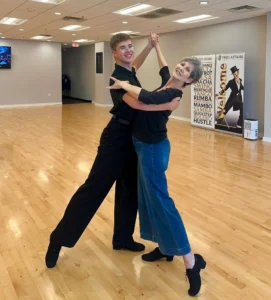 An older woman smiling while dancing with a younger partner in a ballroom studio, showing that it’s never too late to start dancing and overcome the fear, “I'm Too Old to Start Dancing.”