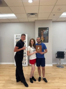 Three adults smiling in a dance studio, holding a bronze dance award, highlighting the joy of learning to dance as a couple at Fred Astaire Dance Studios.