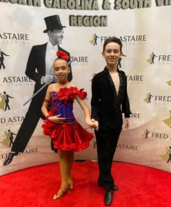 Young ballroom dance partners pose confidently in competition attire at a Fred Astaire Dance Studios event, showing how Performing Can Change Everything by building confidence, stage presence, and dance skills.