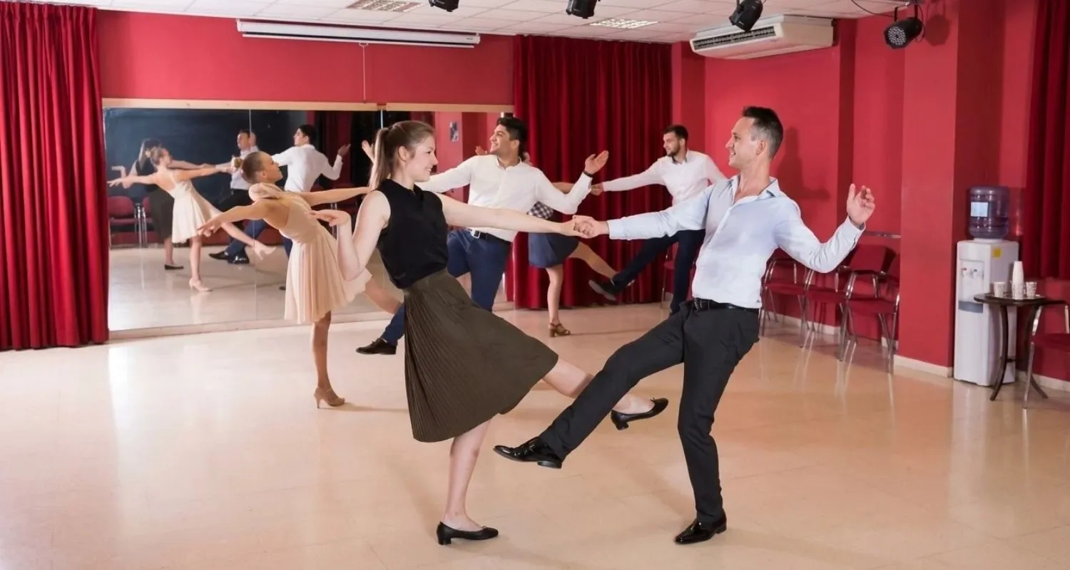A group of dance students in a studio practicing a synchronized leg kick step of East Coast Swing