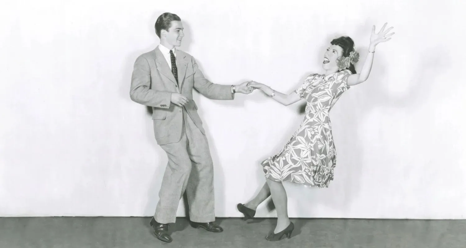 A black and white photograph from the 1940s captures a couple performing a lively East Coast Swing dance move, with the woman being lifted off the ground.