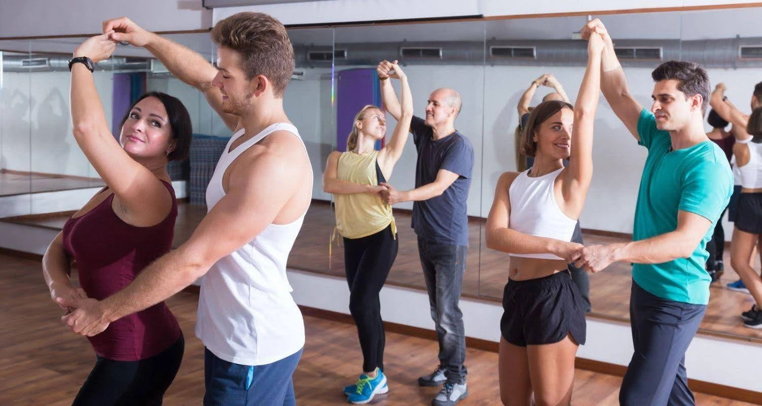 Adults practicing partner turns during a group Latin dance class with rotating partners.