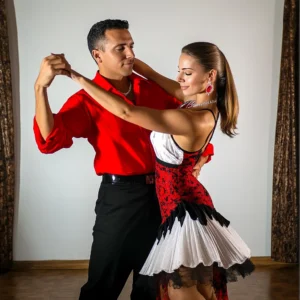 A man in a red shirt and a woman in a red, white, and black dress take Paso Doble dance lessons in Raleigh.