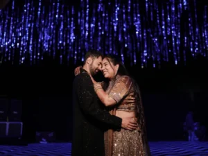 A couple embraces happily under shimmering blue lights. Image complements the blog, Why a Dance Lessons Anniversary Gift Wins Every Time.