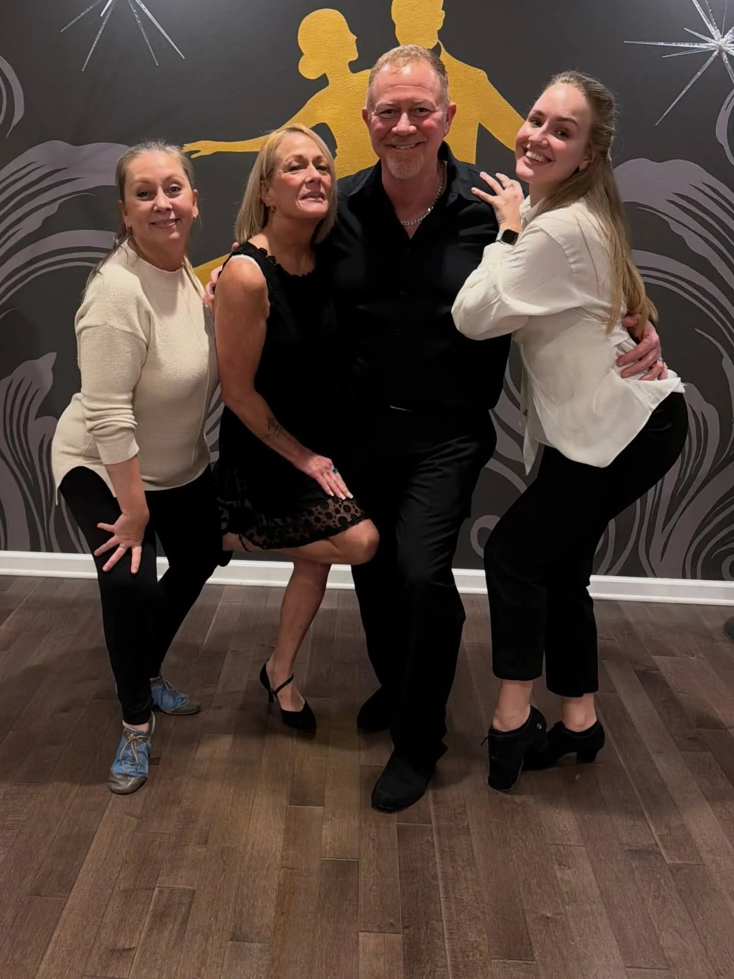 Four dancers pose together in a studio, smiling and enjoying a fun group dance experience that highlights the positive effects of dancing.