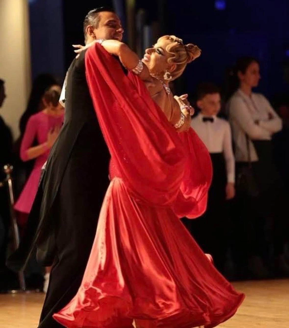 Adult Dance Lessons in West Palm Beach: a ballroom couple glides across the floor, the man in a black tailcoat and the woman in a flowing red gown with sheer cape sleeves.