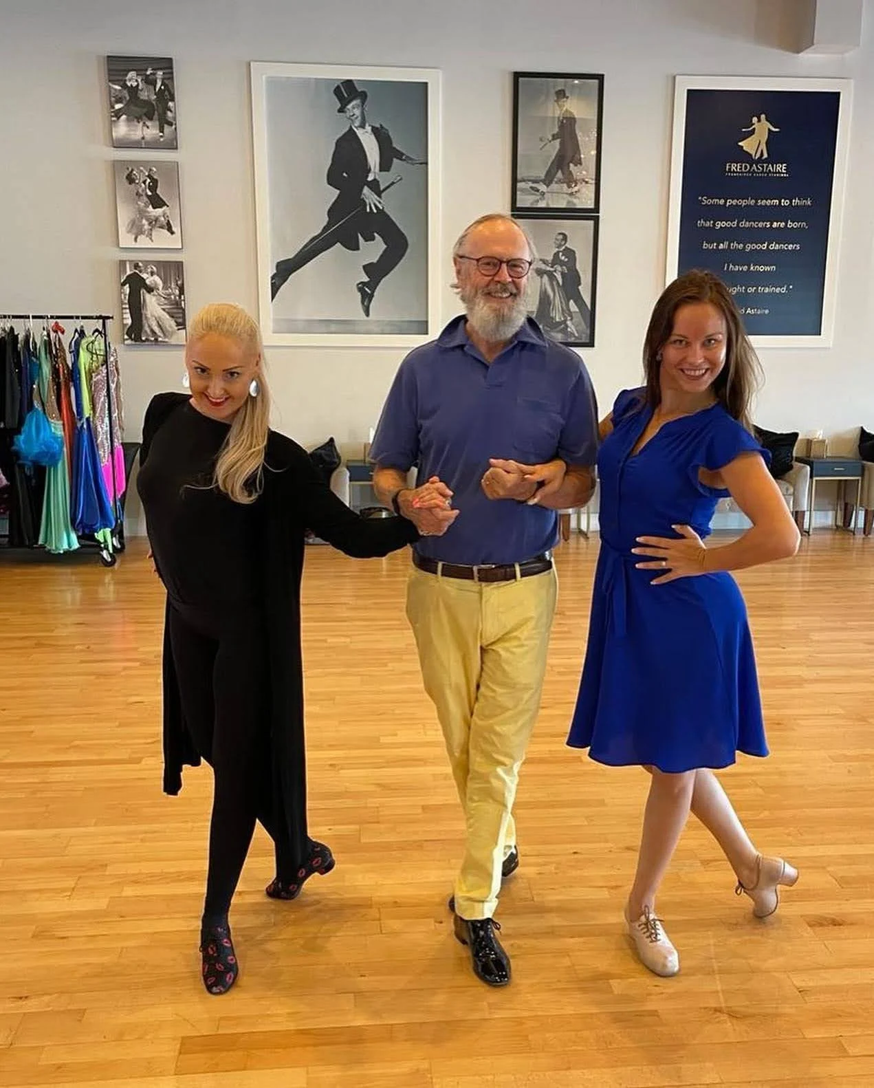 Dance Styles for Beginners: a smiling man links arms with two female instructors in a bright dance studio with black-and-white dance photos on the wall.